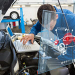 A mechanic in a workshop is analyzing a car engine with the help of advanced digital diagnostic interfaces that display various vehicle metrics and data points, symbolizing the integration of technology in vehicle maintenance.