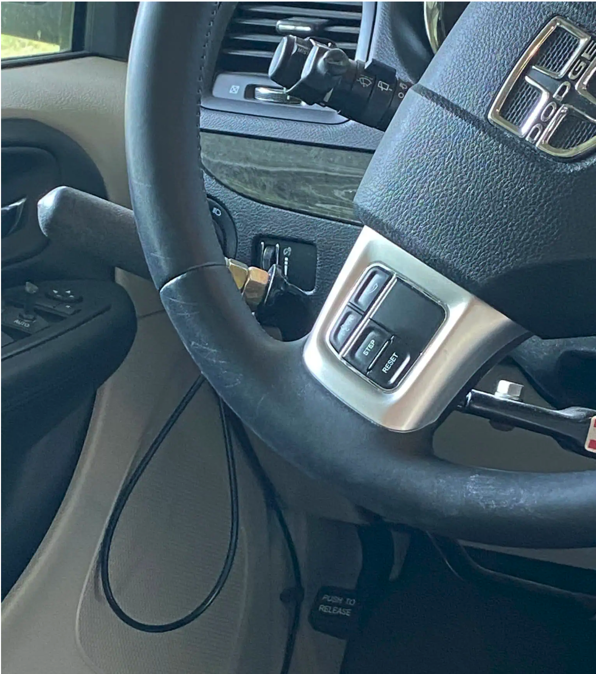 Close-up of a car steering wheel with installed hand controls and cruise control buttons labeled "Step" and "Reset." A lever extends from the wheel, indicating accessibility features.